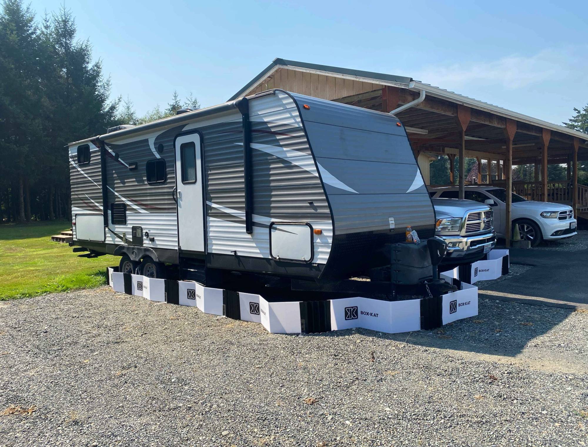 Travel trailer parked inside Box-Kat mouse barrier in front of a wooden building with trees in the background