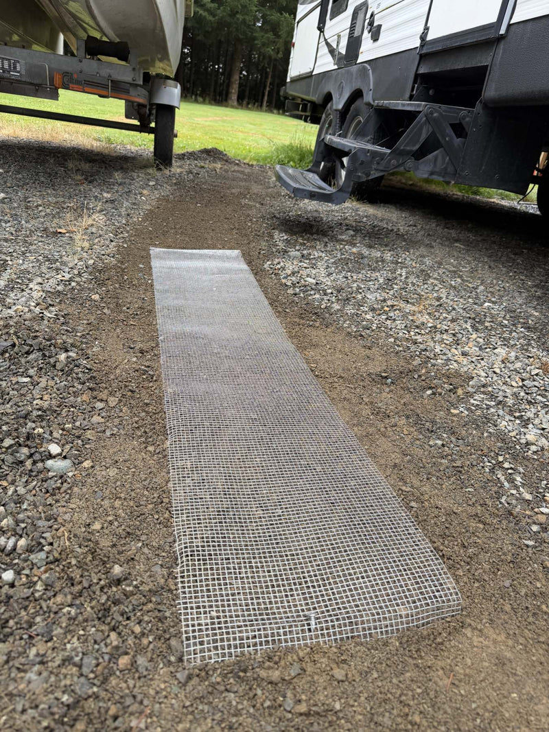 Strip of galvanized wire mesh laid on raked gravel beside a trailer